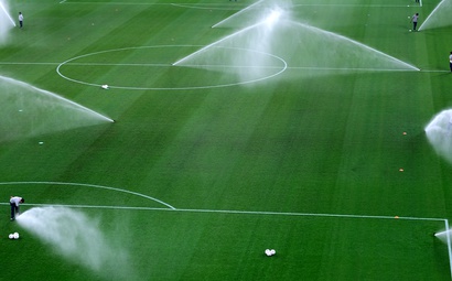 Por que o gramado é irrigado antes do jogo? Grande campo de futebol com o gramado verde, sendo irrigado
