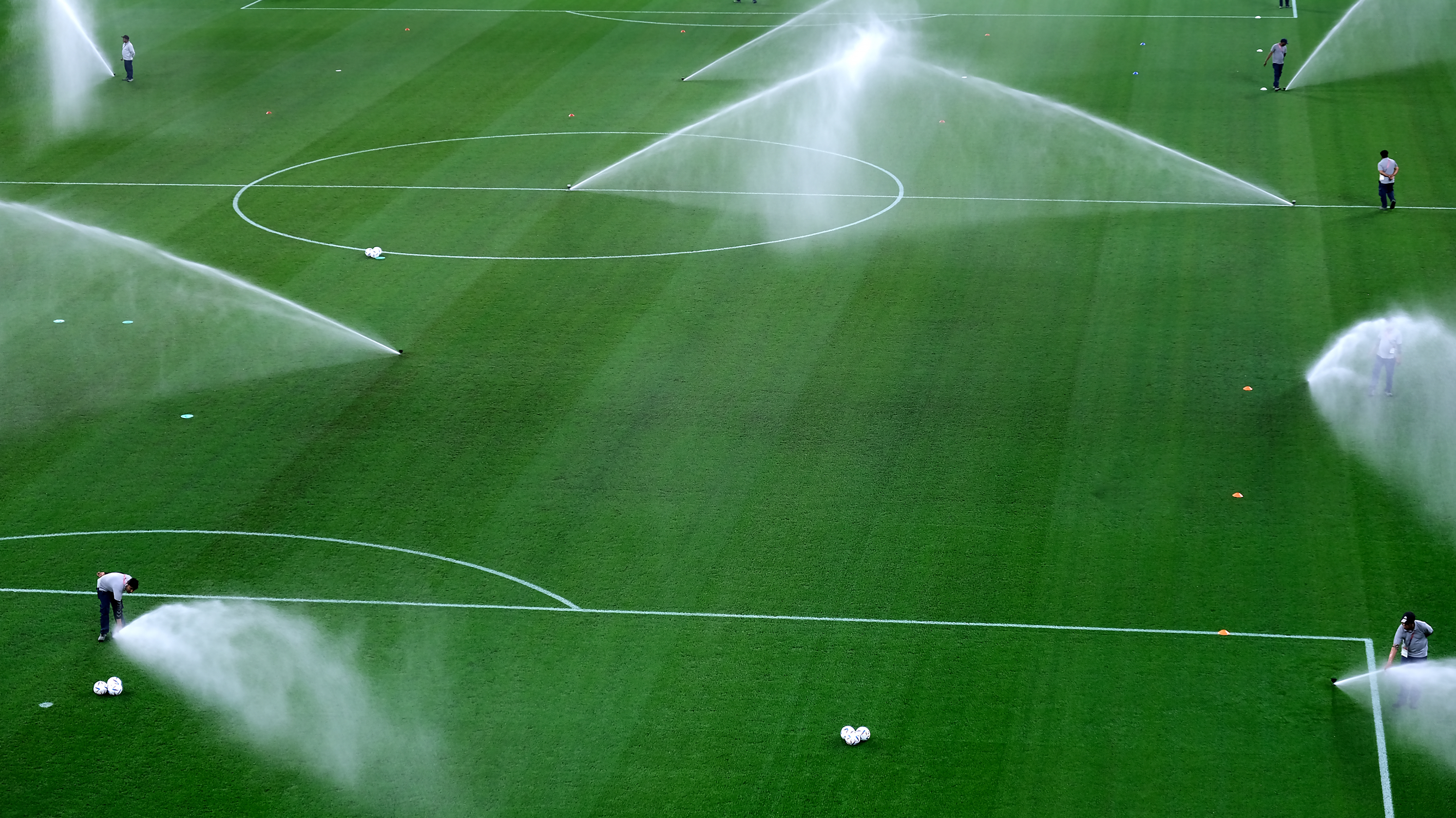 Grande campo de futebol com o gramado verde, sendo irrigado